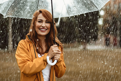 Waist up portrait of laughing pretty woman holding umbrella outdoors. She is looking at camera with sincere smile and delight. Copy space in right side