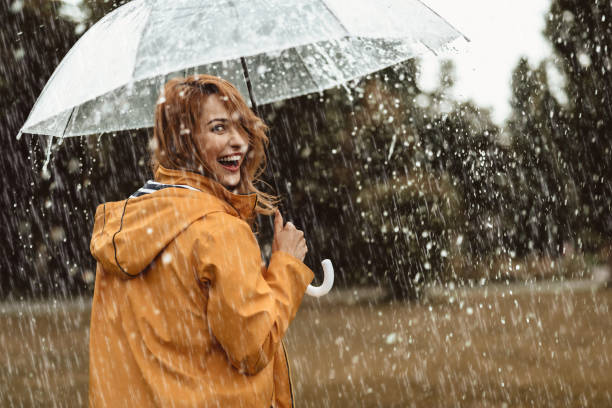 mujer alegre caminando en clima lluvioso - lluvia fotos fotografías e imágenes de stock