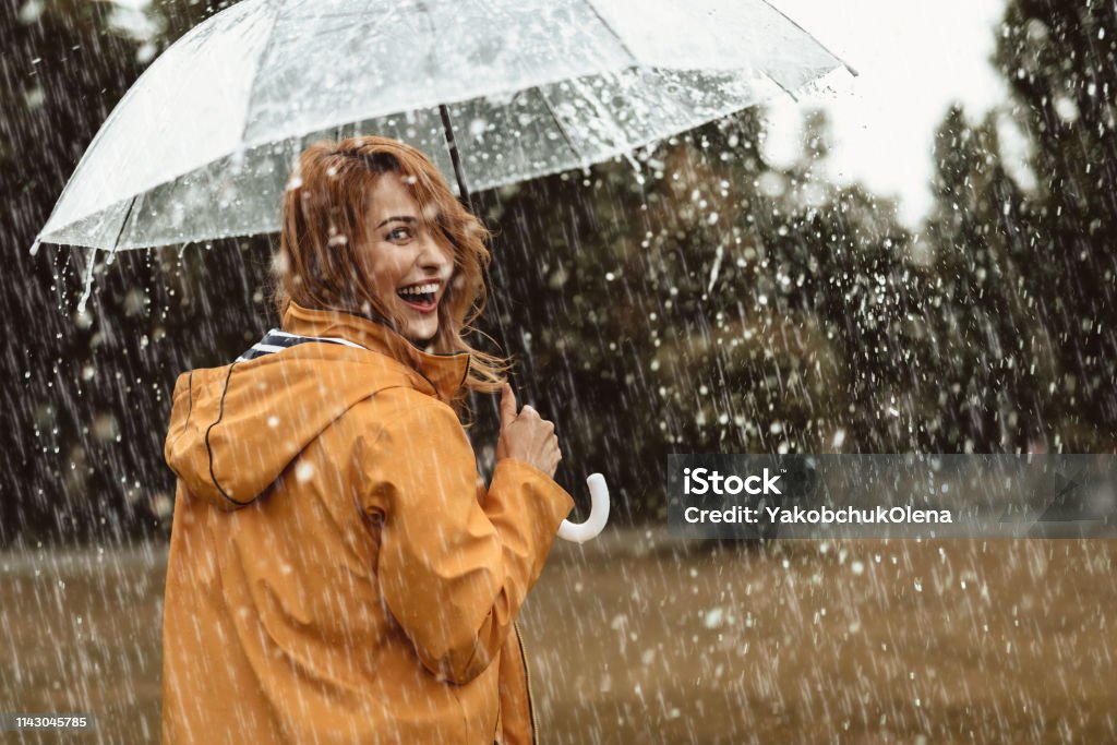 Joyful woman walking in rainy weather Cheerful pretty girl holding umbrella while strolling outside. She is turning back and looking at camera with true delight and sincere smile. Copy space in right side Rain Stock Photo
