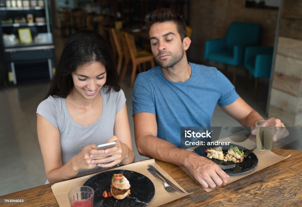 Woman texting at a restaurant and boyfriend trying to see her phone Woman texting at a restaurant and boyfriend trying to see her phone â relationship concepts Envy Stock Photo
