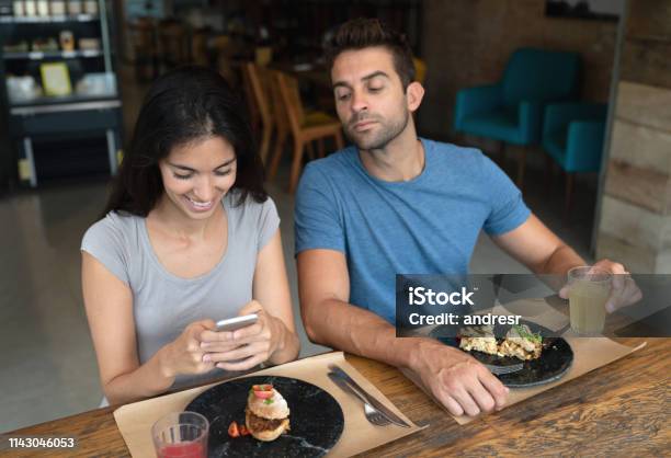 Woman Texting At A Restaurant And Boyfriend Trying To See Her Phone Stock Photo - Download Image Now
