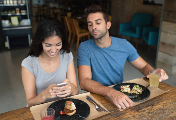 woman texting at a restaurant and boyfriend trying to see her phone - inveja imagens e fotografias de stock