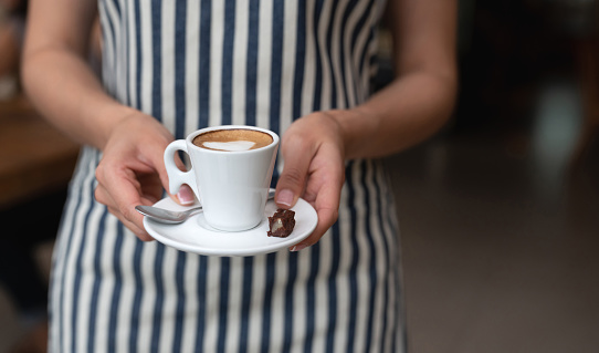 Close-up on a happy waitress serving a cup of coffee at a cafe â lifestyle concepts