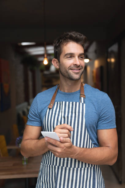 istock Brazilian waiter looking happy at a cafe and holding a notepad 1143046180