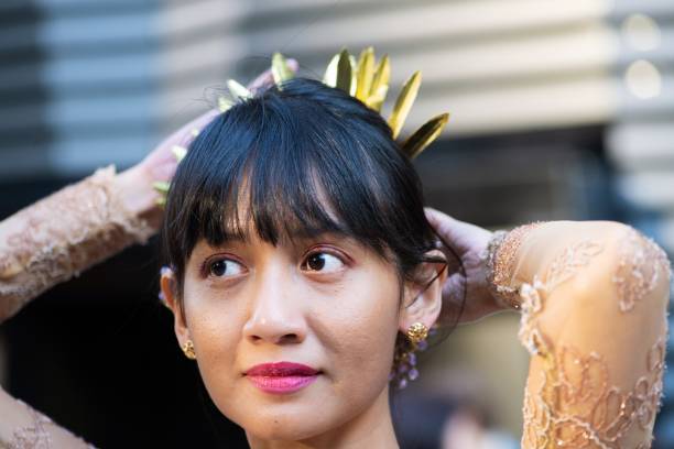 A mid adult woman putting on accessories to match her traditional Indonesian outfit.