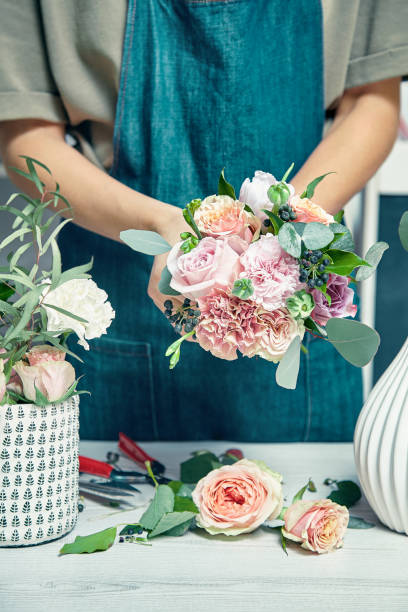 istock Close-up on creative florist work. Female arranging a bouquet with flowers use florist tools standing by workplace in shop. Flowers delivery. Copy space. workplace and professional concept 1143052385