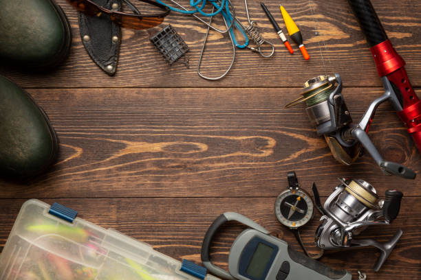 fishing theme. frame with rubber boots, fishing box, reels, fishing buoy, rod, compass, feeder, knife and fish string on wooden background. free space - fishing supplies imagens e fotografias de stock