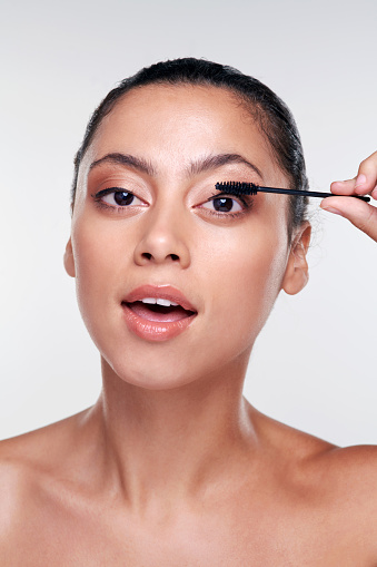 Shot of a beautiful young woman applying mascara  against a studio background