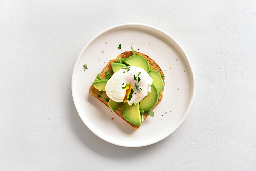 Poached eggs on toasted bread with avocado, rukola and herbs over white stone background with copy space. Top view, flat lay