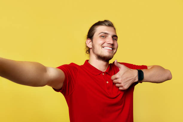 istock Happy-looking young man showing thumb up gesture while taking selfie on yellow background. 1143062214