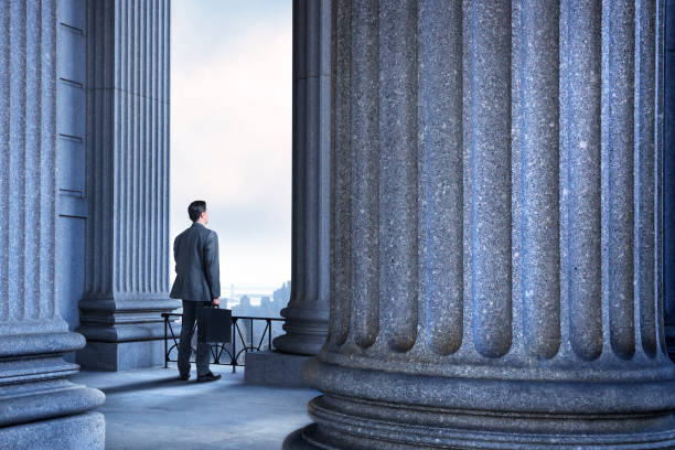 Lawyer Or Businessman Standing In Portico Of Greek Columns A male lawyer or a businessman carrying a briefcase looks into the distance as he stands in a portico of Greek columns that could represent a financial, leagal, or higher learning institution. colonnade stock pictures, royalty-free photos & images