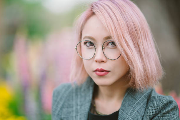 Portrait of beautiful millennial generation woman with pink hair A portrait of a beautiful millennial generation woman with pink hair in front of beautiful flowers. pink hair stock pictures, royalty-free photos & images