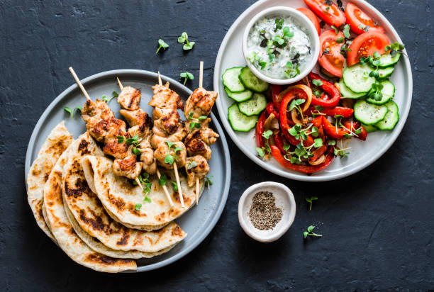 mediterranean style lunch table - turkey skewers, flatbread, tomatoes, cucumber salad, baked sweet pepper, yogurt herb sauce  on a dark background, top view - souvlaki imagens e fotografias de stock