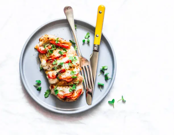 Baked chicken fillet stuffed with tomatoes and mozzarella on a light background, top view