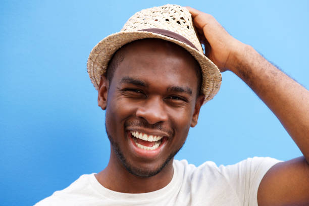 istock Close up cool young black guy with hat smiling against blue background 1143072618