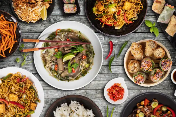 Top view composition of various Asian food in bowls served on wooden table