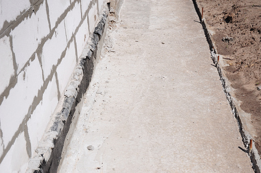 Close up on house foundation waterproofing, damp proofing with contrete path to avoid water leaks for home wall.
