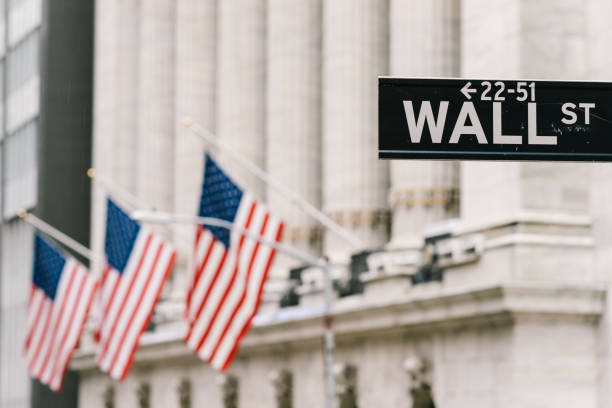 Wall Street sign post with American national flags in background. New York city financial district, stock market trade and exchange, or business concept stock photo