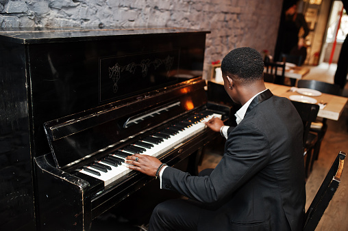 Back of strong powerful african american man in black suit play piano.