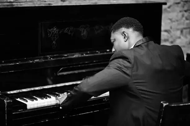 Back of strong powerful african american man in black suit play piano.