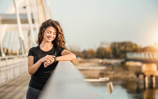 счастливая спортивная молодая женщина, используя смарт-часы. - checking the time watch women looking стоковые фото и изображения