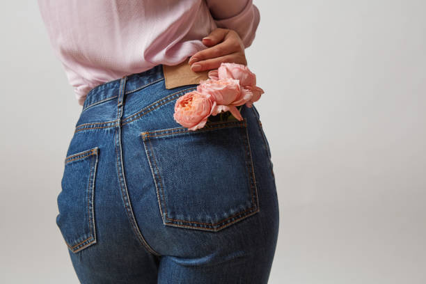 attraktive frau hintern in einer blauen jeans und frische rosen lebende korallenfarbe in einer hinteren tasche auf einem hellgrauen hintergrund, platz für text. glückwunsch karte. - jeans stock-fotos und bilder