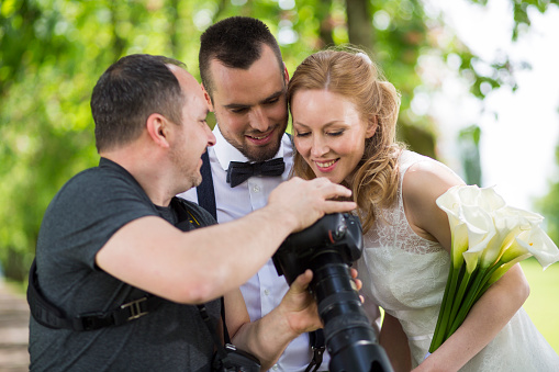 Wedding photographer showing photos on his camera to the newlywed couple in nature.