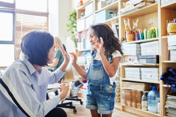 Side view of young female teacher giving high five to adorable girl during art class in school Side view of young female teacher giving high five to adorable girl during art class in school junior level stock pictures, royalty-free photos & images