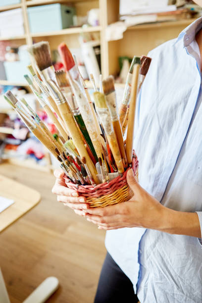 istock Unrecognizable young teacher holding basket with various brushes while standing in classroom in art school 1143087381