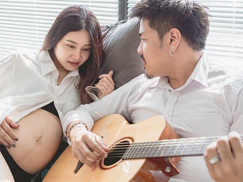 Mom and dad play music and sing a song together. Maternity concept. Pregnancy. Happy family. Expectant mother care. Lovely family. Music day.Man playing acoustic guitar with pregnant woman listen music.