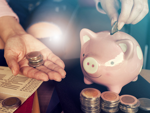 Saving money concept.Close up hand putting coin into piggy bank for saving money.young smart woman holding money coin and prepare to put the coin in piggy bank.