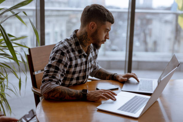 istock Stylish handsome businessman freelancer working by two laptops in cafe 1143093268