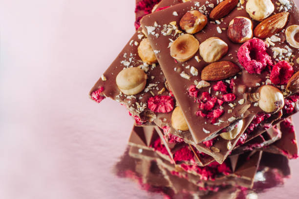 istock Broken handmade chocolate bars with surafce decorated with whole hazelnuts, almond and sublimated raspberry 1143099234