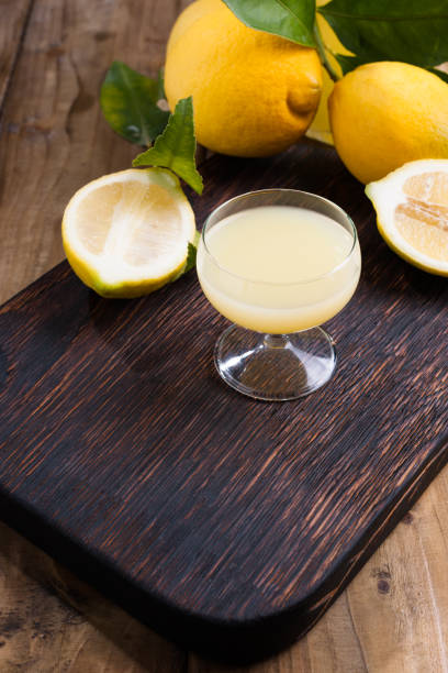 limoncello in un bicchiere e agrumi freschi con foglie verdi. liquore tradizionale italiano al limone. alcol su sfondo di legno scuro. bevande antiche da sud - neapolitan specialty foto e immagini stock