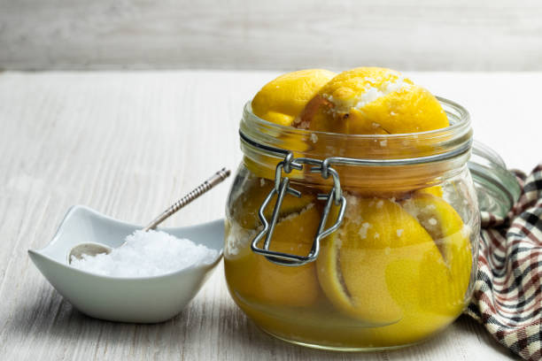 Moroccan preserved salted lemons in glass jar on white wooden table Moroccan preserved salted lemons in glass jar on white wooden table preserved food stock pictures, royalty-free photos & images
