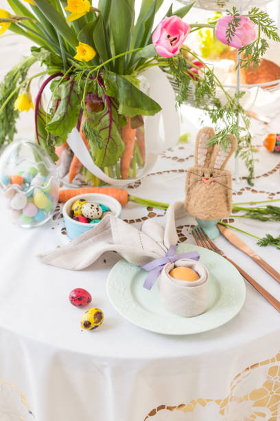 istock Place setting with a painted egg wrapped in a linen napkin shaped like bunny ears on Easter breakfast table. 1143117471