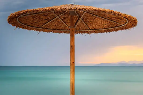 Photo of Colorful sunset view of straw beach parasol and long exposure, smooth sea water