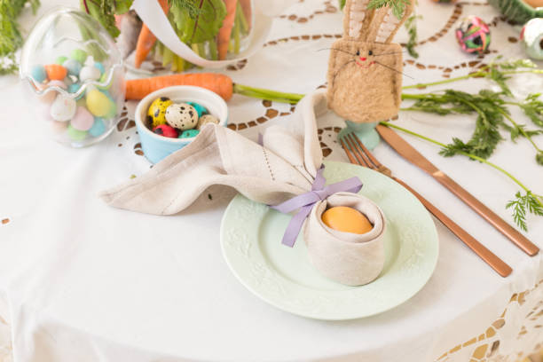 istock Place setting with a painted egg wrapped in a linen napkin shaped like bunny ears on Easter breakfast table. 1143118459