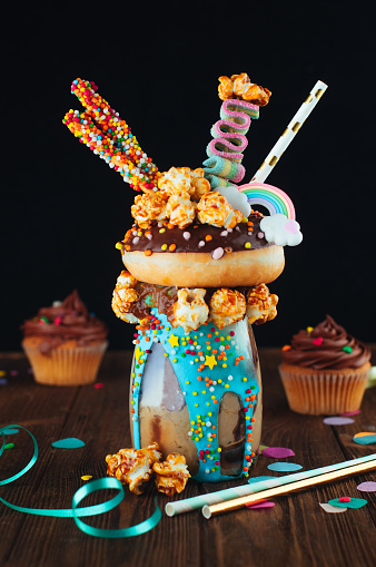 Chocolate freak shake topping with donut and caramel popcorn on the rustic wooden background; selective focus.