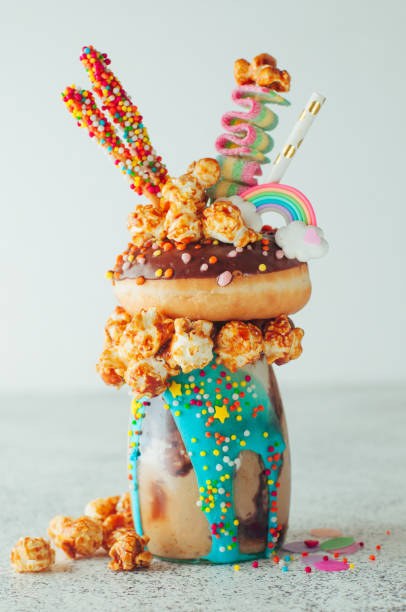 Chocolate freak shake topping with donut and caramel popcorn on the party table Chocolate freak shake topping with donut and caramel popcorn with sweets and straw; selective focus. milkshake photos stock pictures, royalty-free photos & images