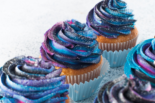 Close up of vanilla cupcake with colorful galaxy whipped cream. Selective focus.