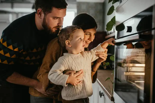 Young family with son is looking in the oven and waiting for their meal to be done.