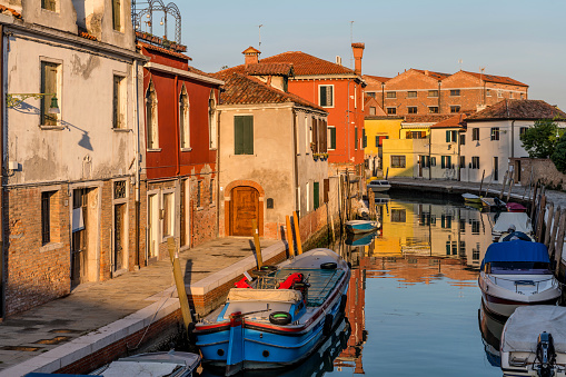 Sunset view of a narrow, old, but colorful canal on Murano Islands. Venice, Italy. No recognizable trademark, logo, sign or person in this image. The main subject of the image is the narrow but colorful canal.