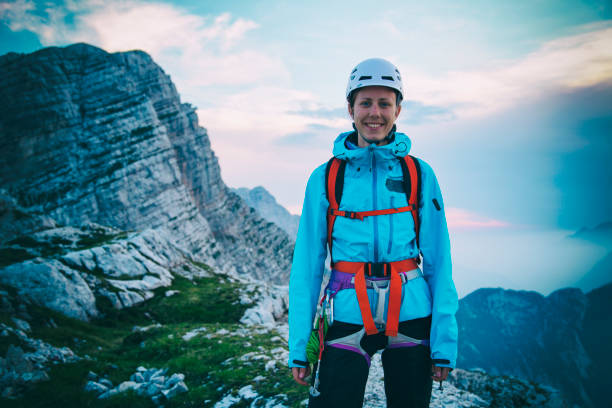 Young woman in mountain climbing gear standing on the top of the mountain with a smile on her face. Evening mood.