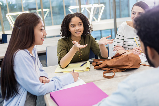 Diverse college students participate in a study group. A female student gestures as she talks withe a mal student.