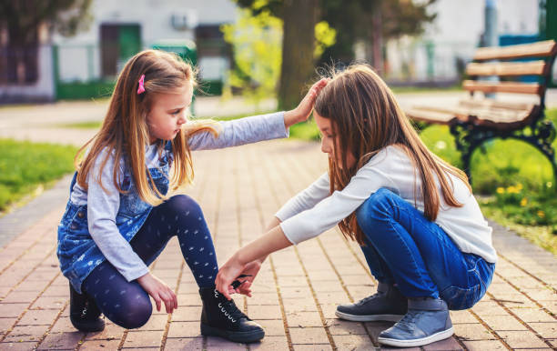 Help and care for a friend. Girl tying shoes of another little girl stock photo