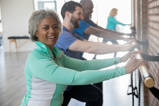 Happy senior woman exercising in barre class with personal trainer