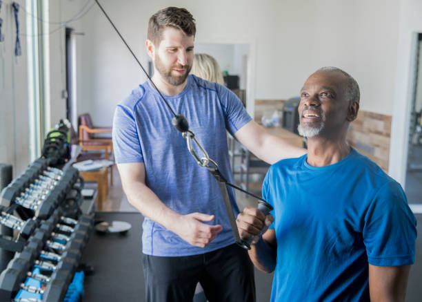 レジスタンスウェイトトレーニングでシニアクライアントを支援するパーソナルトレーナー - men weight training african descent male ストックフォトと画像