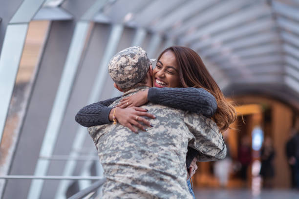 A beautiful woman of Indian descent passionately hugs her partner as she greets him returning from his military service. He is wearing a military uniform.