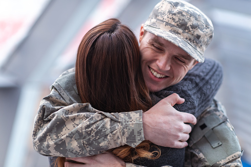 A handsome man dressed in a military uniform passionately hugs his partner as he greets her returning from his military service in this close-up.